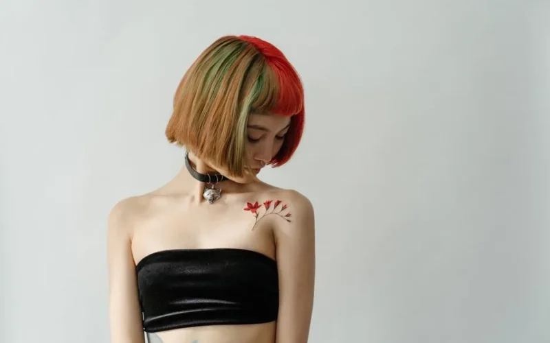 Asian woman with vibrant hair and shoulder tattoo in a studio setting.