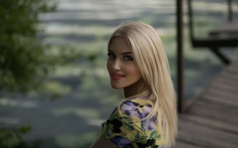 Relaxed portrait of a blonde woman smiling by a lake in Prague, capturing the essence of summer serenity.