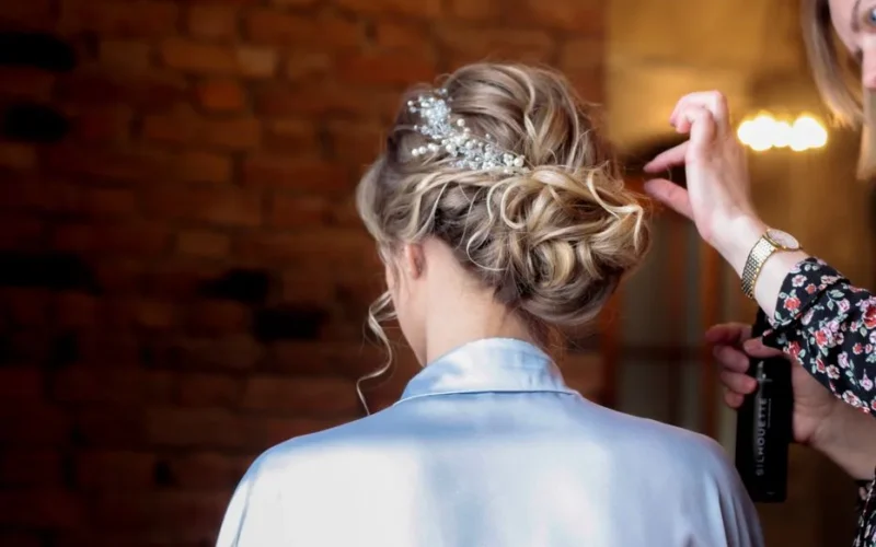Bridal hairstyling with intricate updo and headpiece being perfected for the wedding day.