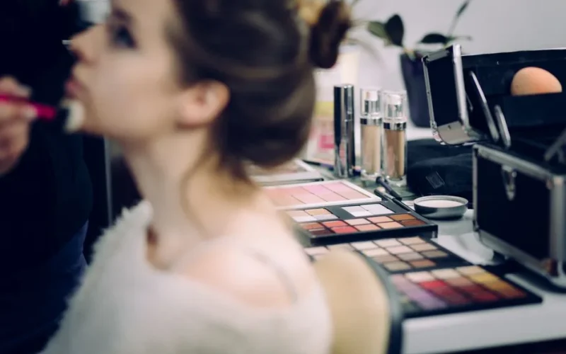 A woman receiving professional makeup in a studio with various cosmetics in focus.