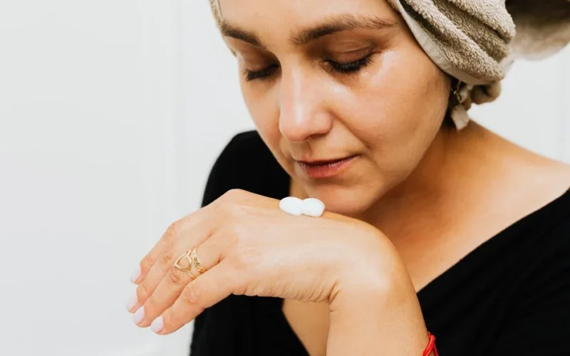 Close-up of a woman applying skincare cream to hand, promoting self-care.
