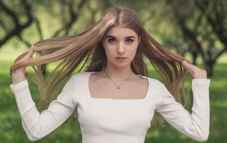 Portrait of a young woman outdoors holding her long hair, in a green park setting.