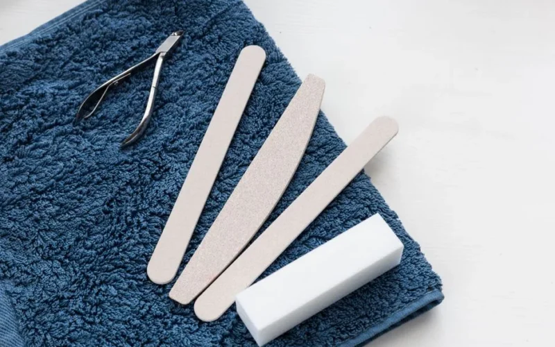 A neatly arranged manicure toolkit with cuticle nipper and nail files on a soft blue towel, ideal for salons.