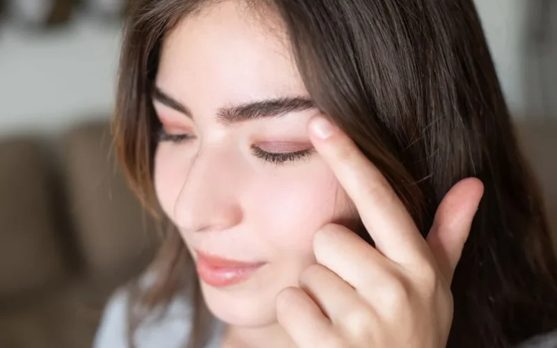 Close-up portrait of a woman touching her eyelid showcasing natural eye makeup.