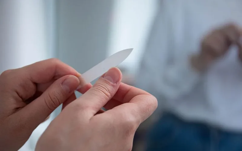 A person uses a glass nail file to groom their nails, reflecting self-care and grooming habits.