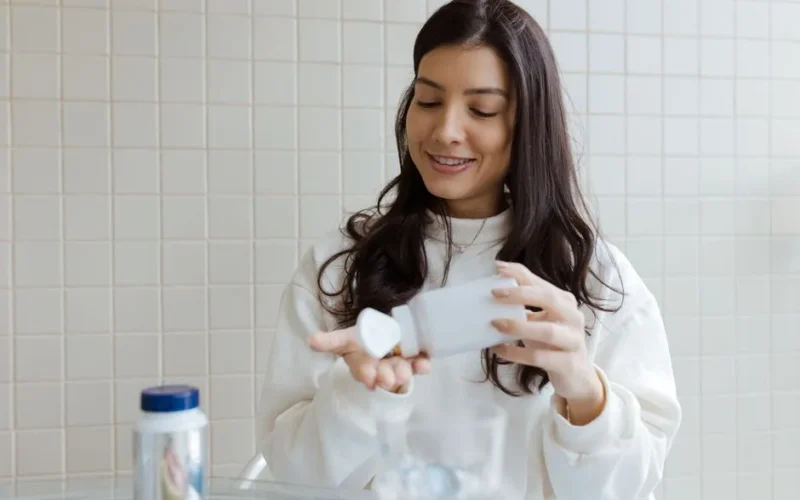 A woman smiles as she pours pills from a bottle into her hand, capturing a healthcare moment.
