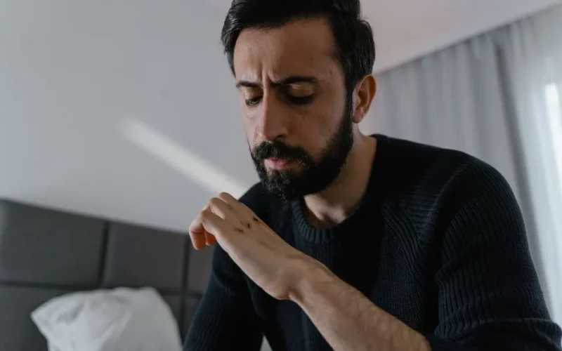 A thoughtful man closely examines a wound on his hand while indoors.