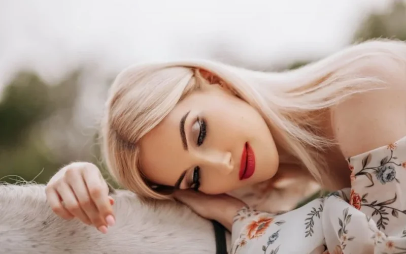 Blonde woman in floral dress rests outdoors, serene and relaxed.
