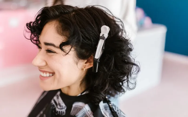 Side profile of a woman with curly hair smiling in a hair salon with a hair clip.