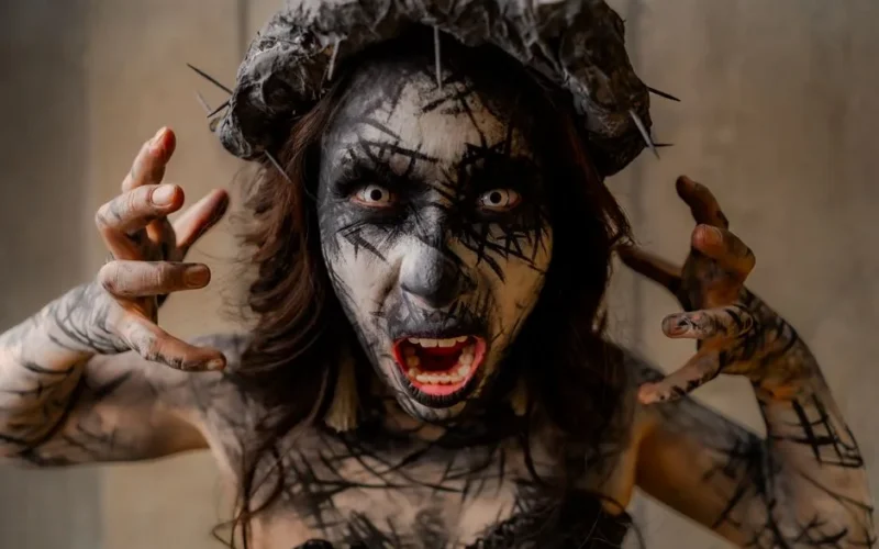 A dramatic portrait of a person with surreal horror makeup and a spiked headpiece, evoking a gothic atmosphere.