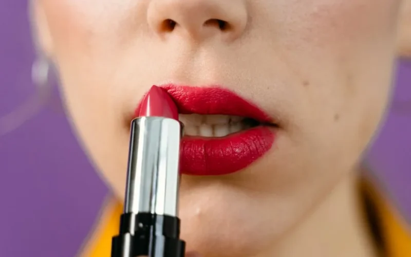 Detailed view of a woman applying vibrant red lipstick on her lips.