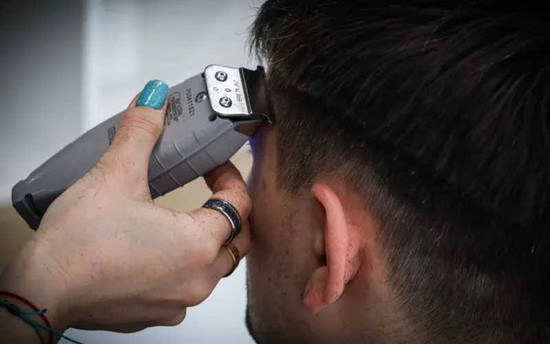 Detailed view of a haircut in progress with electric clippers and stylist's hand.