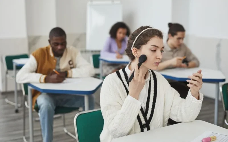 Students in a classroom setting, focusing on studying and makeup application.