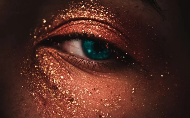 A stunning close-up of a human eye adorned with gold glitter makeup, showcasing beauty and fashion.