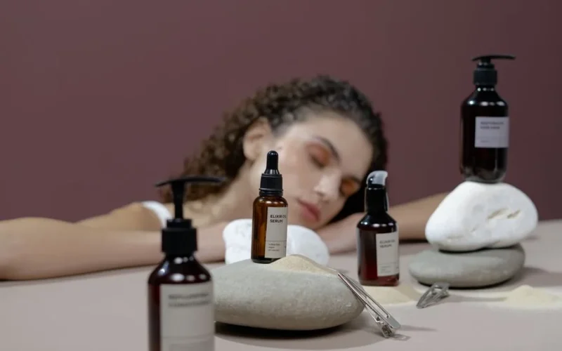 Woman with curly hair surrounded by natural stones and haircare products, eyes closed.