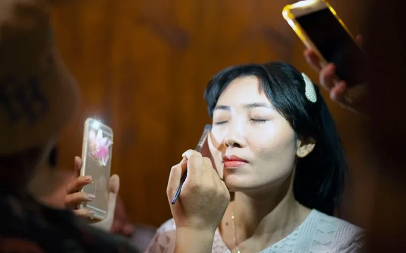 Woman getting makeup applied under smartphone light indoors.