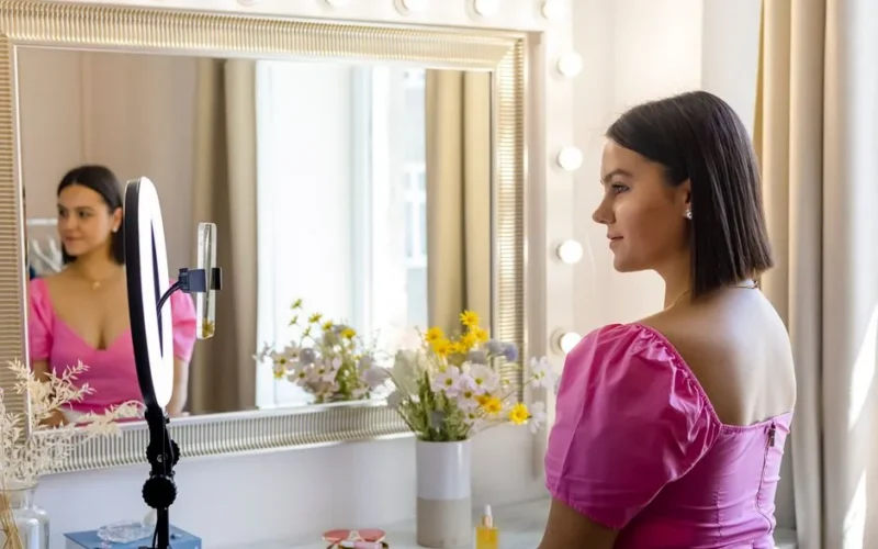 A young woman records a vlog using a ring light in front of a stylish mirror.