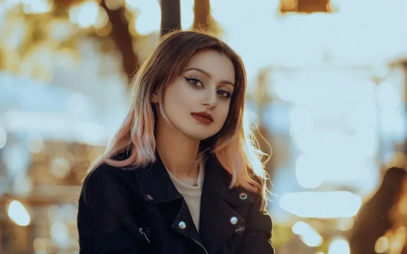 Charming portrait of a young woman with stylish makeup and jacket in sunlight.