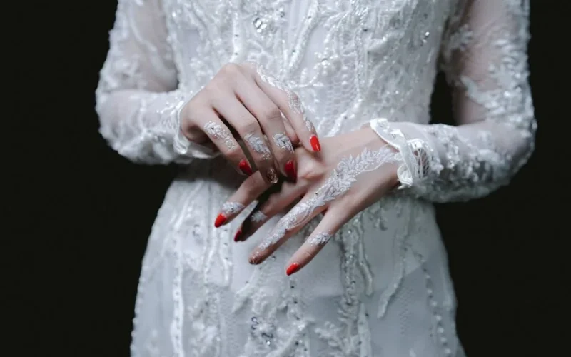 Close-up of elegantly manicured bridal hands with lace detail, showcasing intricate wedding design.