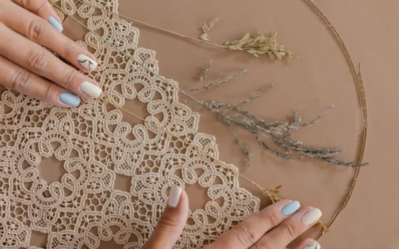 A close-up of handmade lace creation with delicate hands and colorful nails, showcasing intricate craftsmanship.