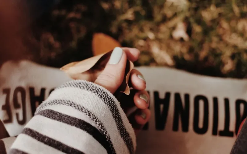 Close-up of a woman's manicured hand holding autumn leaves, conveying warmth and coziness.