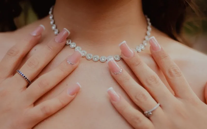 Close-up of elegant diamond necklace and manicured hands, showcasing jewelry fashion and style.