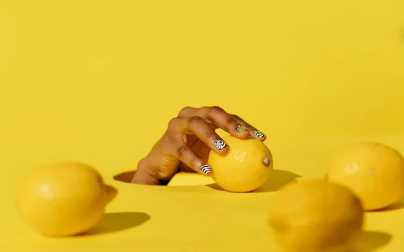Striking yellow lemons held by a hand with stylish nail art, set against a vibrant lemon-colored backdrop.