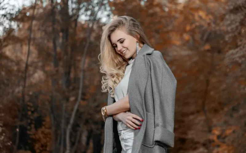 Blonde woman with a fashionable coat enjoying a serene autumn day outdoors.