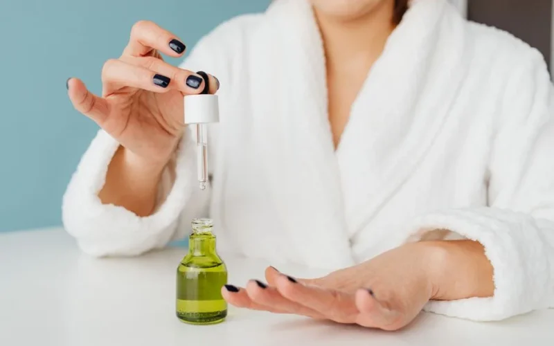 Close-up of a woman in a bathrobe using a dropper to apply serum to her hand.
