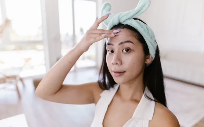 A young woman applies skincare products at home, emphasizing her daily beauty routine.