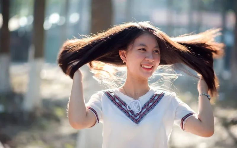 Joyful woman enjoying a sunny day while playfully lifting her hair outdoors.