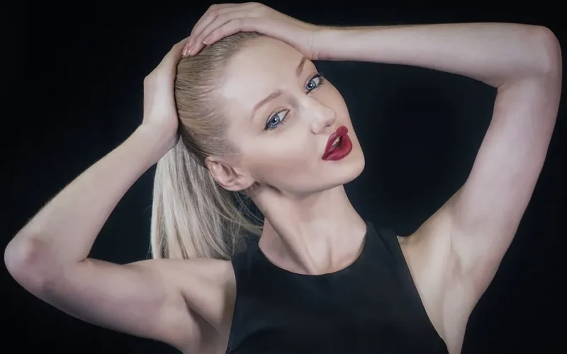 Close-up portrait of a stylish woman with red lips and a sleek ponytail, striking a pose.