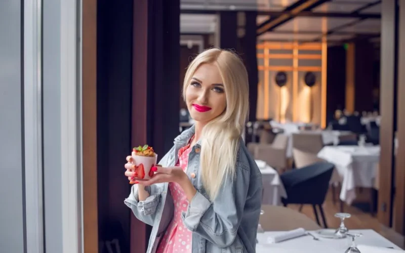 Blonde woman in a chic Parisian restaurant savoring a stylish dessert.