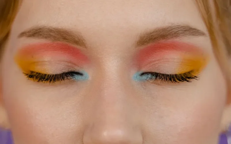 Close-up of a woman's closed eyes showcasing vibrant multicolored eye makeup.