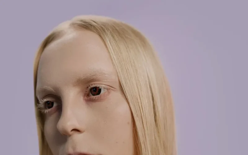 Close-up of a person with blonde hair and a light purple background.