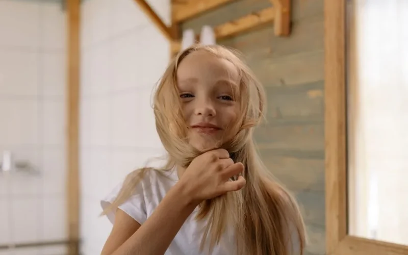 Playful portrait of a blonde girl smiling as she twists her hair indoors.