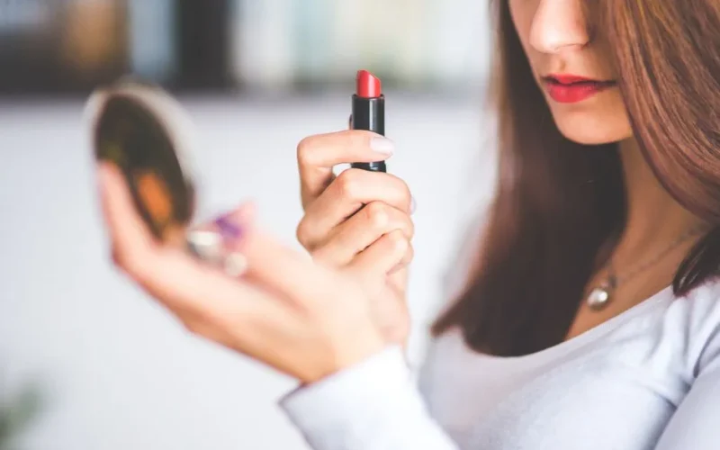 Close-up of woman applying red lipstick while holding a compact mirror.