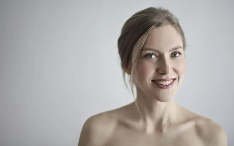 Close-up portrait of a smiling blonde woman against a gray background, embodying elegance and beauty.