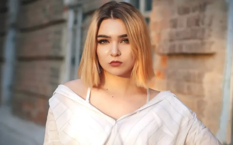 Close-up portrait of a woman wearing a white shirt standing outdoors against a brick wall.