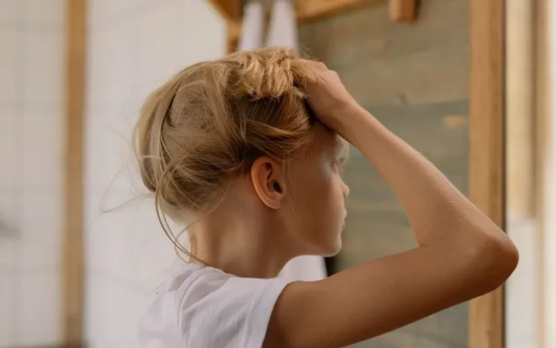 Blonde girl adjusting hair in front of a mirror with soft lighting.