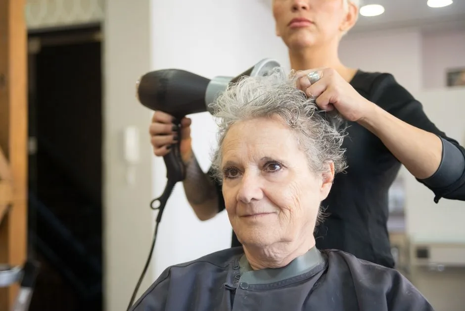 Elderly woman with white hair receiving a blow-dry at a hair salon in Portugal.
